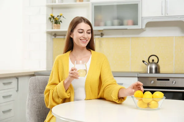 Mujer joven con vaso de agua de limón en la cocina — Foto de Stock