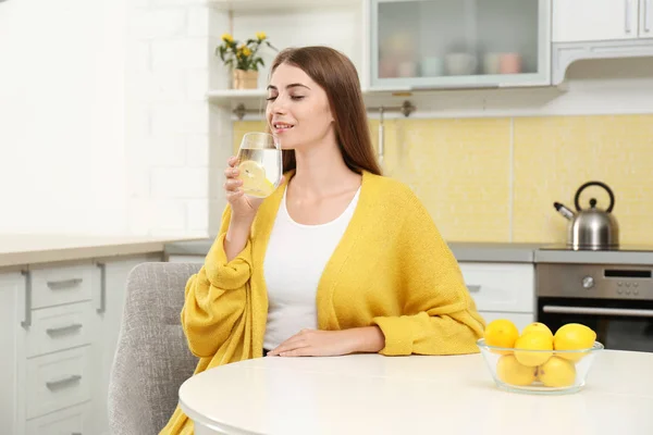 Молодая женщина пьет лимонную воду на кухне — стоковое фото