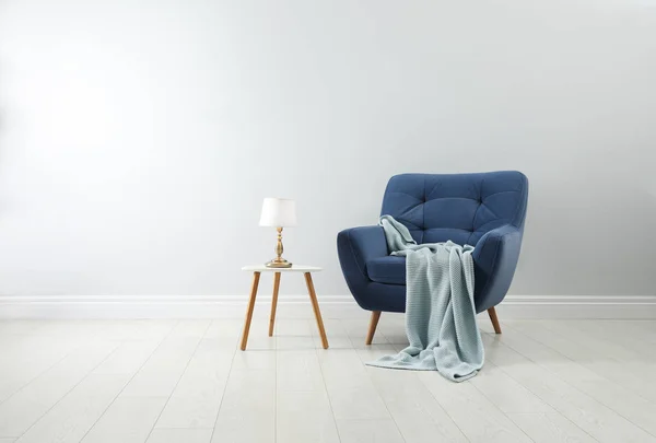 Stijlvolle fauteuil met plaid, tafel en lamp in de buurt van witte muur. Int — Stockfoto