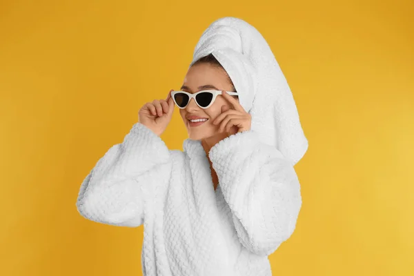 Piękna młoda kobieta w szlafroku i okularach przeciwsłonecznych na żółtym tle — Zdjęcie stockowe