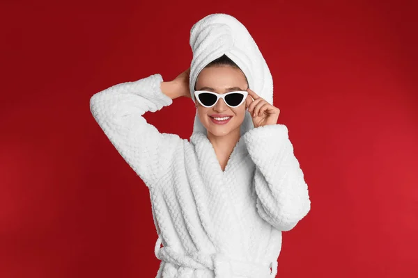 Mooie jonge vrouw in badjas en zonnebril op rode achtergrond — Stockfoto