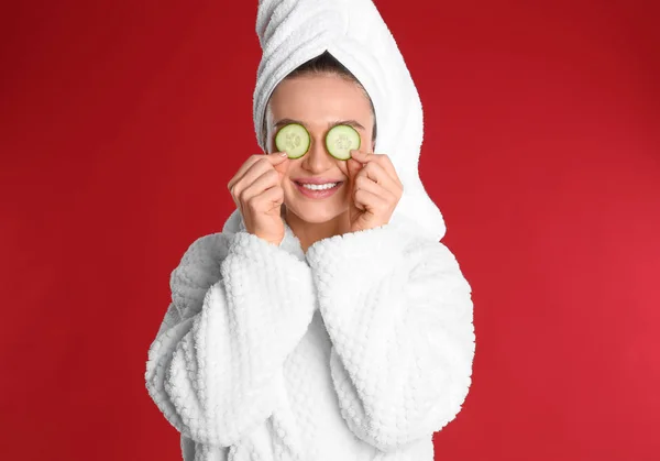 Fiatal nő fürdőköpenyben uborka szeletek piros háttér — Stock Fotó