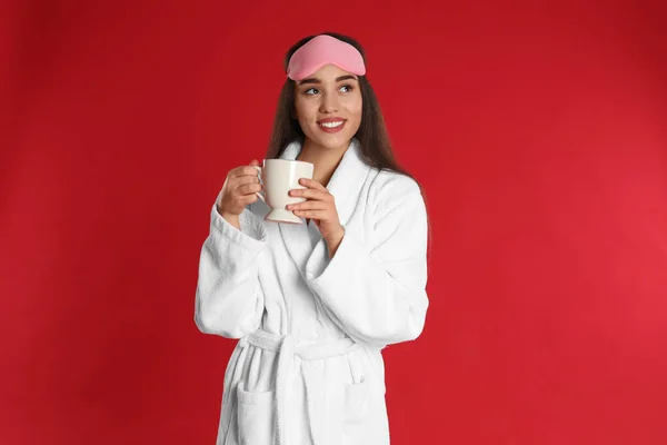 Jovem mulher em roupão de banho com xícara de café no fundo vermelho — Fotografia de Stock