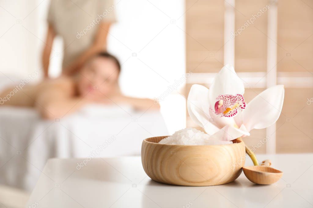 Bowl with sea salt and orchid flower on white table in spa salon