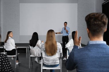 Erkek işletme eğitmeni konferans odasında projeksiyon ekranıyla konferans veriyor.