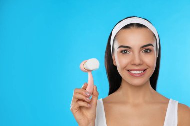 Açık mavi arka planda yüz temizleme fırçası tutan genç bir kadın. Mesaj için yer var. Yıkama aksesuarı