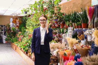 Kadın işyeri sahibi çiçekçide cep telefonuyla konuşuyor.