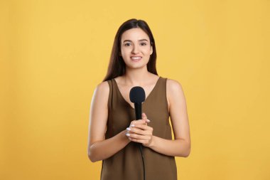 Sarı arka planda mikrofonu olan genç bayan gazeteci.