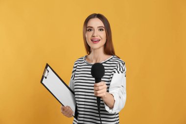 Sarı arka planda mikrofonu ve panosu olan genç bir kadın gazeteci.