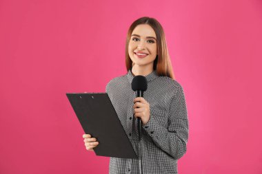 Pembe arka planda mikrofonu ve panosu olan genç bir kadın gazeteci.
