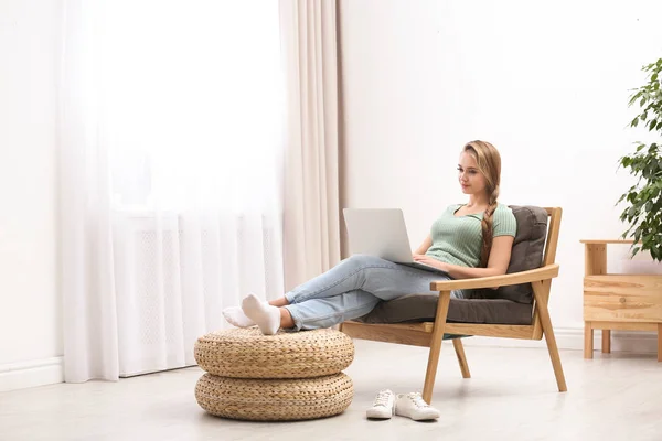 Giovane donna con computer portatile seduta in poltrona a casa — Foto Stock