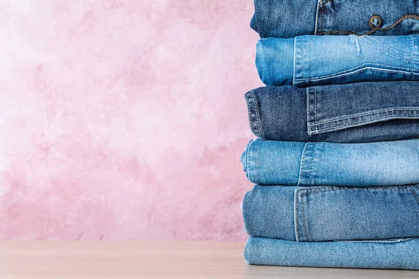 Ahşap Masada Pembe Arka Plana Karşı Farklı Kot Pantolon Yığını — Stok fotoğraf