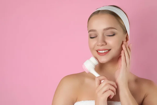 Jovem mulher lavar rosto com escova de limpeza no fundo rosa — Fotografia de Stock