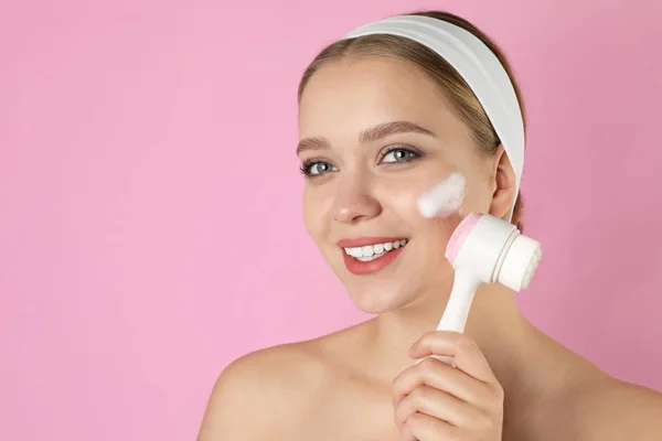 Giovane donna lavaggio viso con pennello e schiuma detergente rosa b — Foto Stock