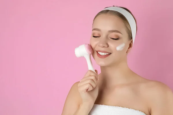 Jovem mulher lavar rosto com escova e espuma de limpeza em rosa b — Fotografia de Stock