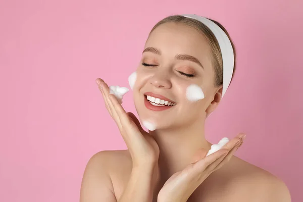 Jovem mulher lavar rosto com espuma de limpeza no fundo rosa . — Fotografia de Stock