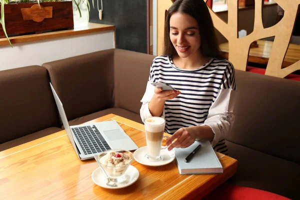 Jonge blogger neemt foto van dessert en latte aan tafel in van — Stockfoto