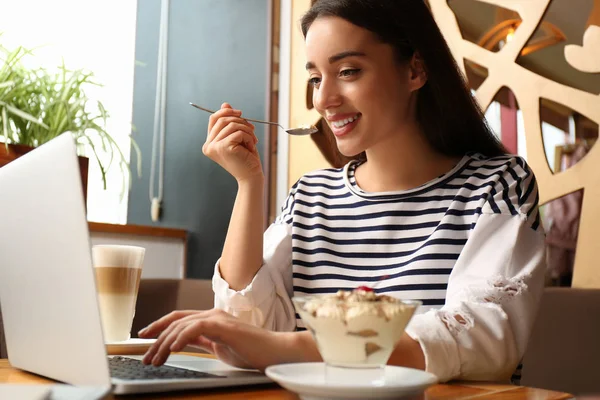 Young blogger with laptop eating dessert in cafe — ストック写真