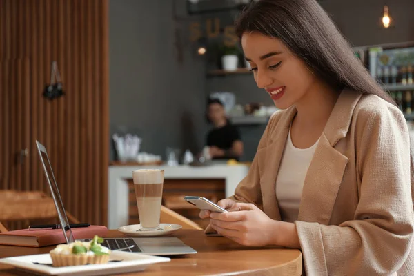 Kafede akıllı telefonu ve dizüstü bilgisayarı olan genç bir blog yazarı — Stok fotoğraf