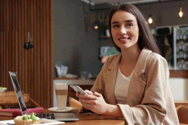 Kafede akıllı telefonu ve dizüstü bilgisayarı olan genç bir blog yazarı — Stok fotoğraf