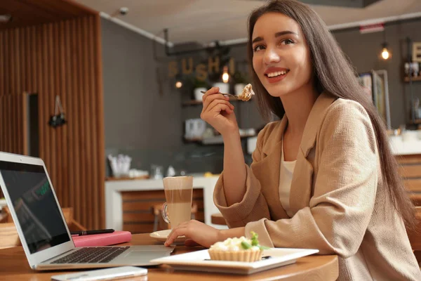 Молодой блогер с ноутбуком ест торт в кафе — стоковое фото