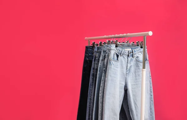 Rack with stylish jeans on pink background, closeup. Space for t — Stock Photo, Image