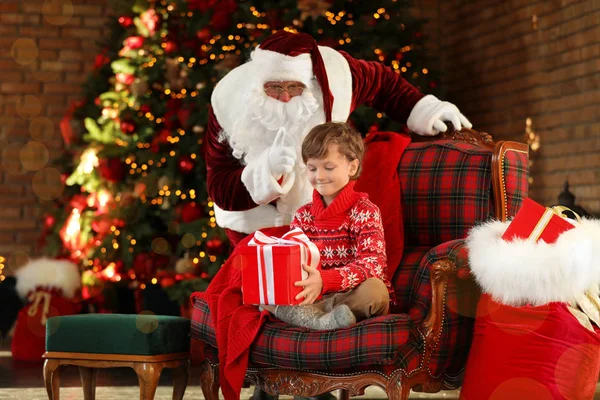 Santa Claus a malý chlapec s dárkem v blízkosti vánočního stromečku uvnitř — Stock fotografie