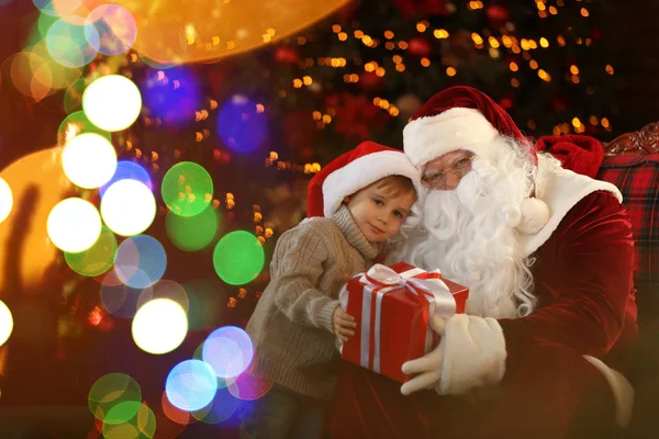 Papá Noel y niño pequeño con regalo cerca del árbol de Navidad en el interior — Foto de Stock