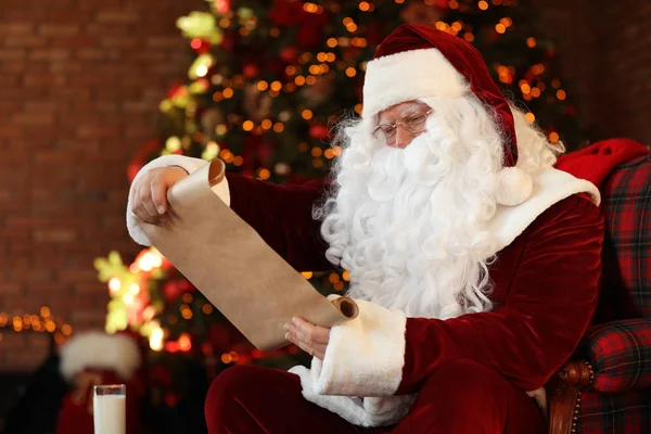 Санта-Клаус со списком пожеланий возле елки в помещении — стоковое фото
