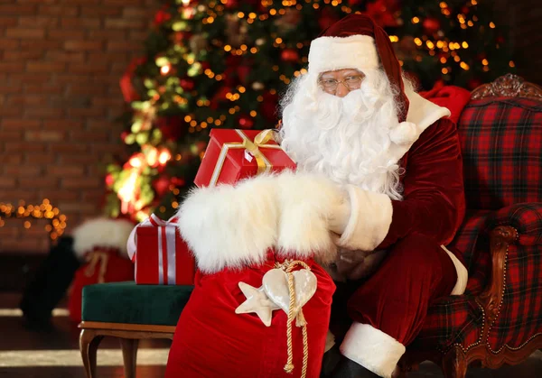 Санта-Клаус с подарочным мешком возле елки в помещении — стоковое фото