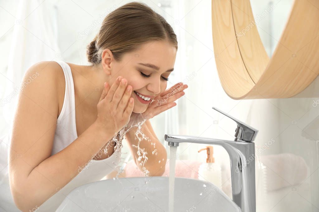 Young woman washing face with tap water in bathroom