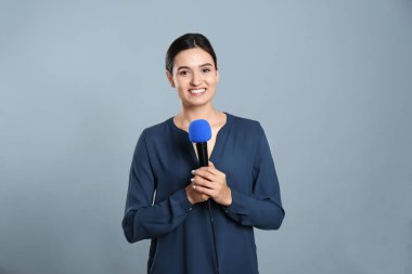 Gri arka planda mikrofonu olan genç bayan gazeteci.