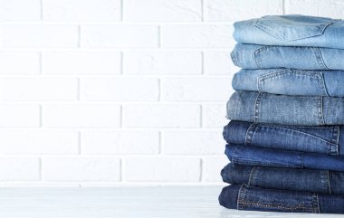 Tuğla duvara karşı beyaz ahşap masada farklı kot pantolon yığını. Metin için boşluk
