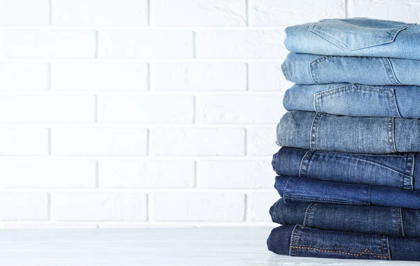 Stapel Verschillende Jeans Witte Houten Tafel Tegen Bakstenen Muur Ruimte — Stockfoto