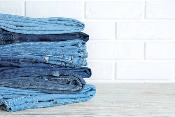 Stack Olika Jeans Vitt Träbord Mot Tegelvägg Plats För Text — Stockfoto