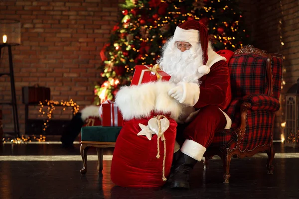 Weihnachtsmann mit Geschenksack neben Weihnachtsbaum drinnen — Stockfoto