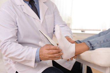 Male orthopedist fitting insole on patient's foot in clinic, closeup clipart