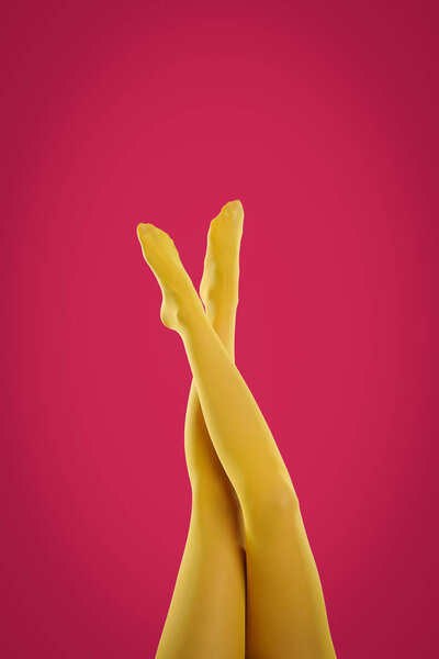 Woman wearing yellow tights on crimson background, closeup of legs