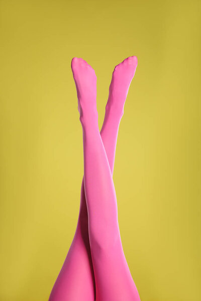 Woman wearing pink tights on yellow background, closeup of legs