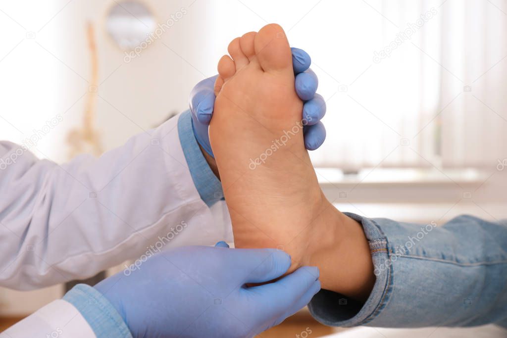 Male orthopedist checking patient's foot in clinic, closeup