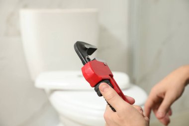 Profesyonel tesisatçı banyoda tuvalet deliğinin yanında boru anahtarı tutuyor.
