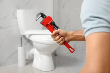 Profesyonel tesisatçı banyoda tuvalet deliğinin yanında boru anahtarı tutuyor.