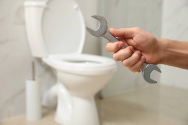 Profesyonel tesisatçı banyoda tuvalet deliğinin yanında ingiliz anahtarı tutuyor.