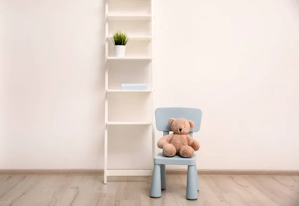 Медвежонок на стуле и полке возле стены в детской комнате — стоковое фото