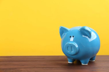 Sarı arka planda, ahşap masanın üzerinde mavi domuz kumbarası. Metin için boşluk