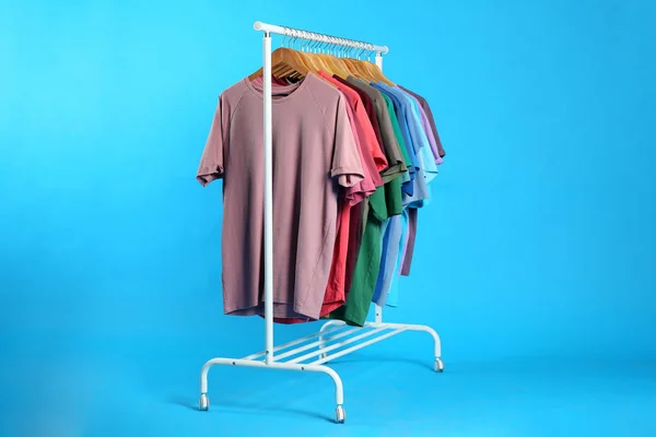 Farbenfrohe Kleidung Die Auf Einem Regal Vor Hellblauem Hintergrund Hängt — Stockfoto