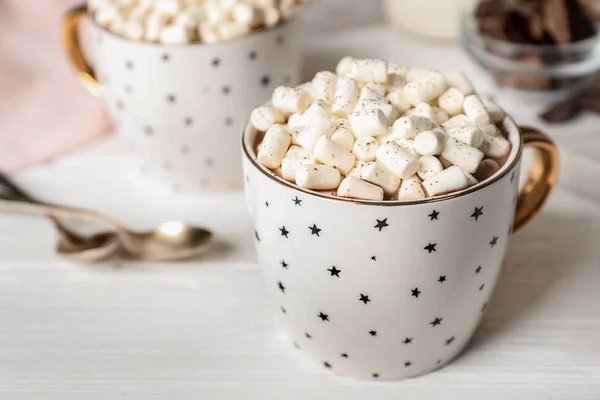 Delicious cocoa drink with marshmallows in cup on white wooden table, space for text