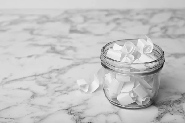 Tarro de vidrio con piezas de papel sobre mesa de mármol blanco, espacio para tex — Foto de Stock