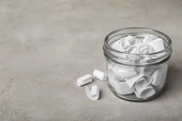 Glazen pot met papieren stukken op grijze tafel, ruimte voor tekst — Stockfoto