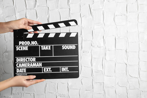 Woman holding clapperboard against white textured wall, closeup with space for text. Cinema production